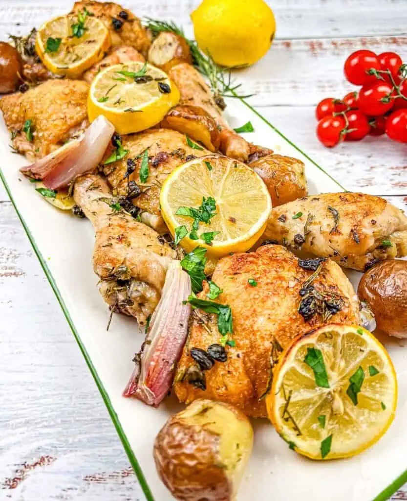 Roasted chicken with lemons and potatoes on a white plate.