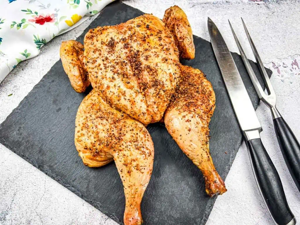 Roasted chicken on a slate board with carving knife and fork.