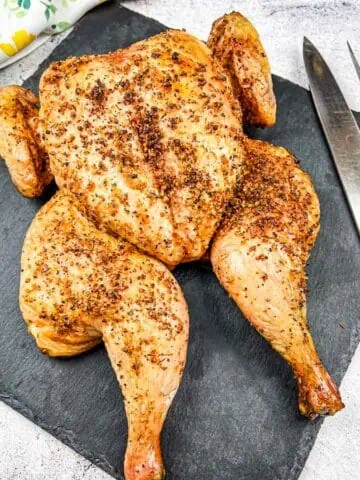 Roasted chicken on a slate board with carving knife and fork.