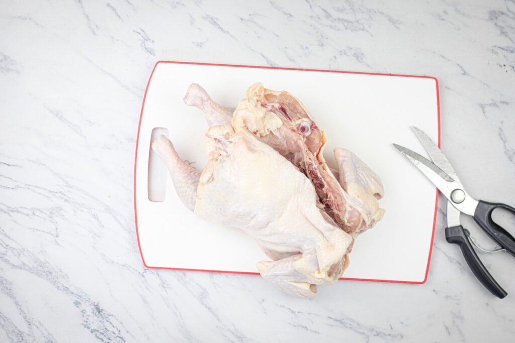 Raw whole chicken on a red cutting board next to kitchen shears.