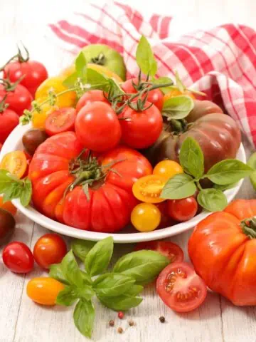 A variety of fresh tomatoes with basil on a wooden table.