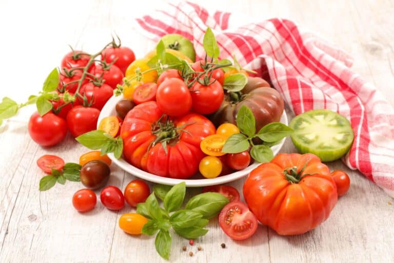 A variety of fresh tomatoes with basil on a wooden table.