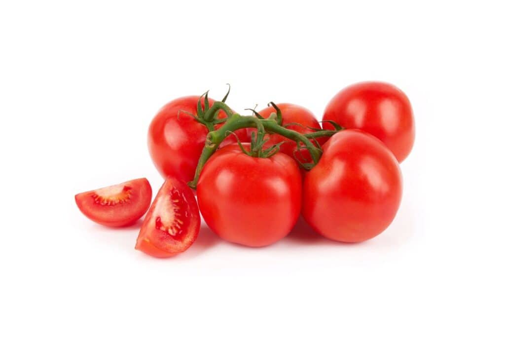 A cluster of ripe red tomatoes with one tomato sliced on a white background.
