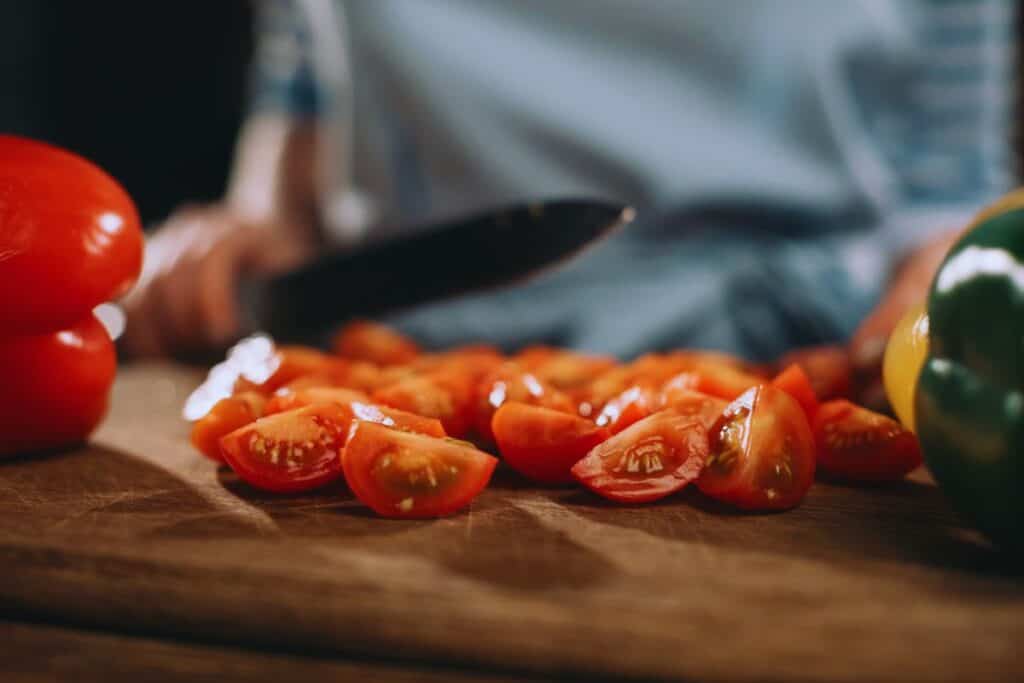 Person slicing cherry tomatoes on a wooden cutting board with vegetables nearby.