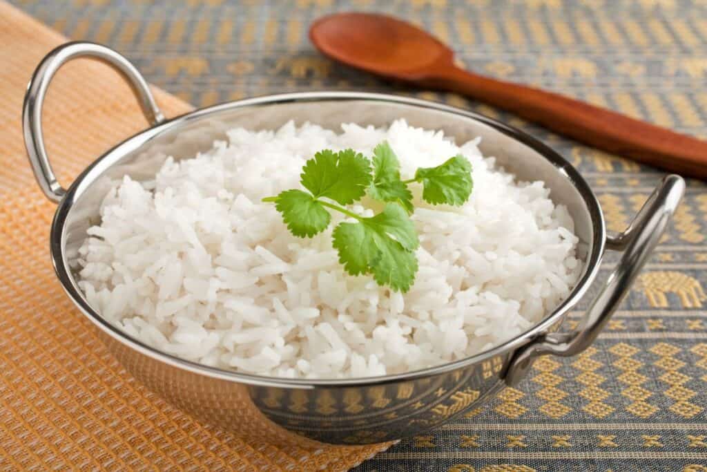 A bowl of cooked white rice garnished with a cilantro leaf, accompanied by a wooden spoon.