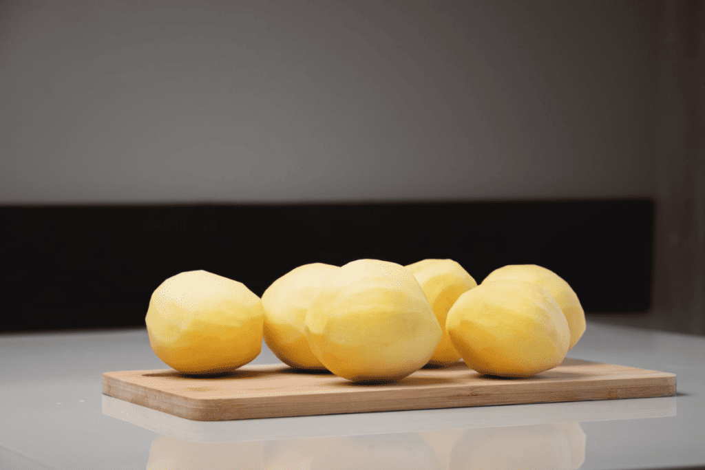 Four potatoes on a wooden cutting board.
