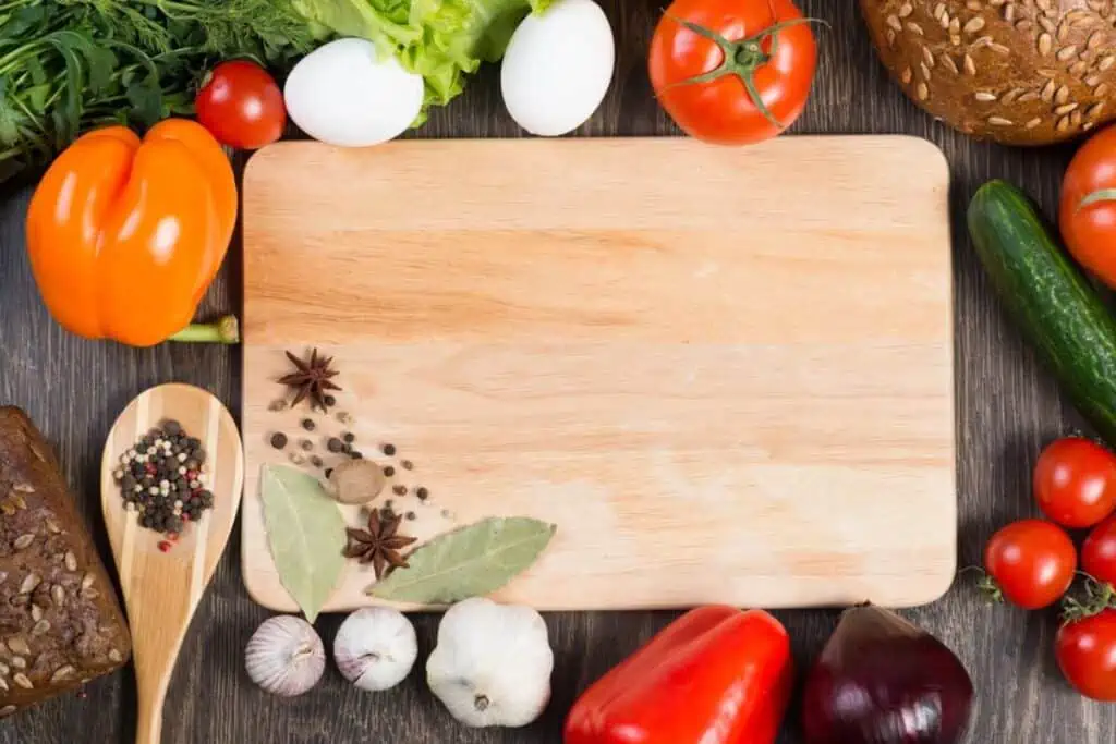 A wooden cutting board surrounded by vegetables and herbs.
