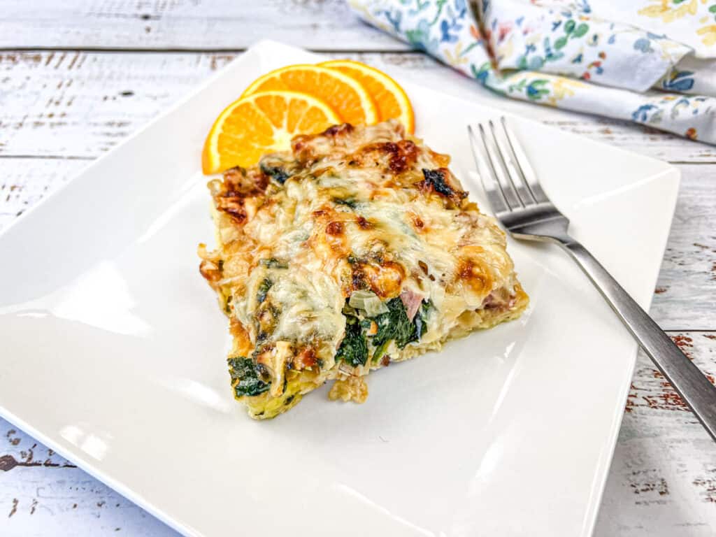 A slice of breakfast casserole on a white plate with orange slices.
