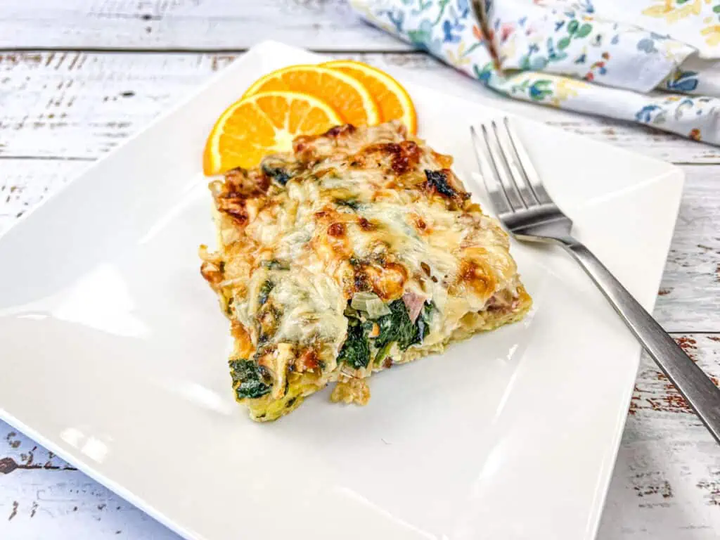 A slice of breakfast casserole on a white plate with orange slices.