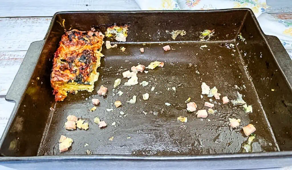 A nearly empty baking tray with remnants of a fall casserole and a single slice remaining.