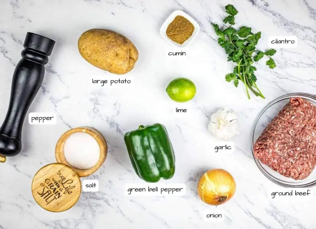 Ingredients for a recipe laid out on a marble countertop including spices, vegetables, and ground beef.