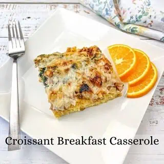 A slice of croissant breakfast casserole served on a white plate with orange slices on the side.