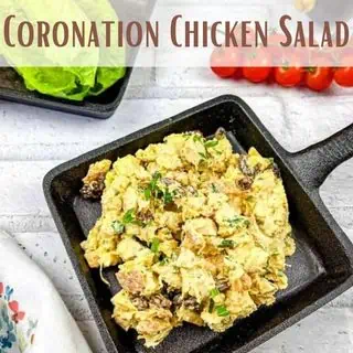 Coronation chicken salad served in a black skillet, with fresh tomatoes and lettuce on the side.