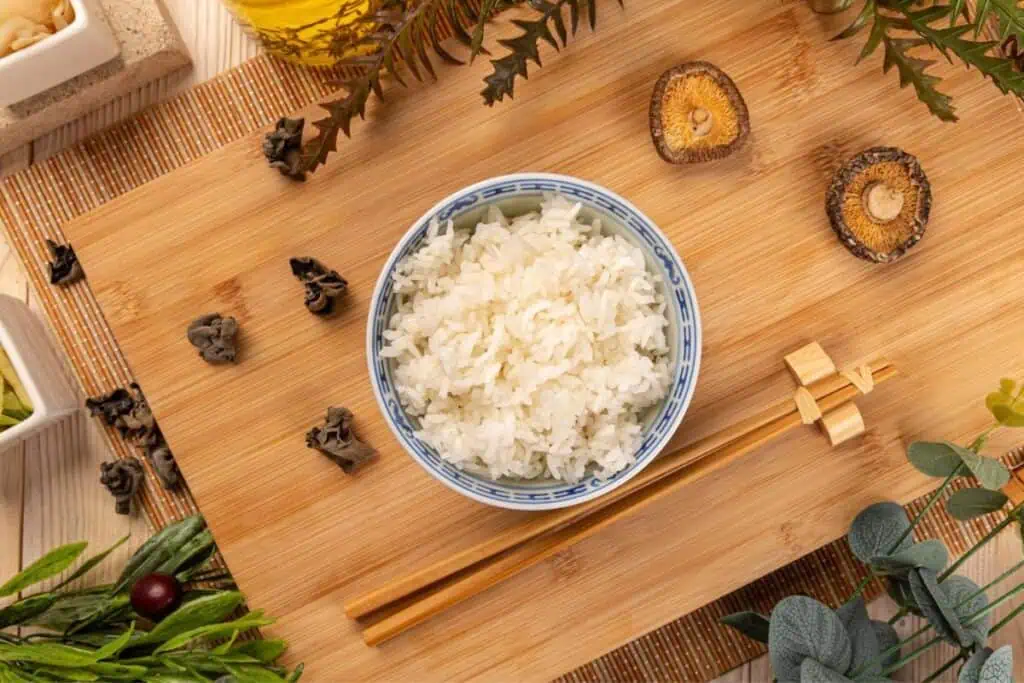 A bowl of steamed rice on a bamboo mat surrounded by asian-inspired decor.