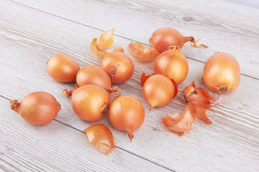 A group of whole yellow onions with papery skins on a wooden surface.