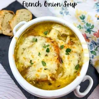 A bowl of french onion soup topped with melted cheese and garnished with herbs, served with slices of bread on the side.