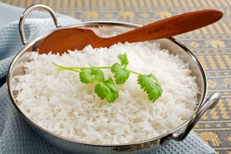 Basmati rice in a steel karahi, garnished with coriander, with a wooden spoon.