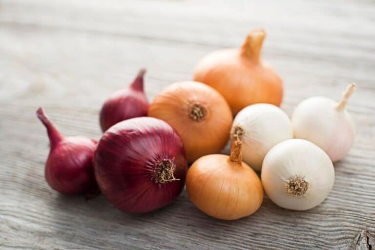Assorted onions on a wooden surface.