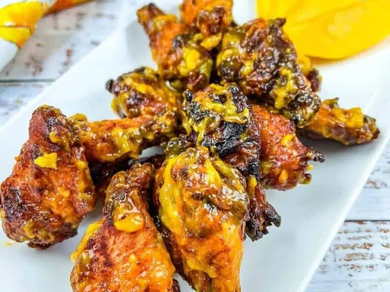 A plate of glazed chicken wings with a slightly charred exterior, served alongside sliced yellow bell peppers.