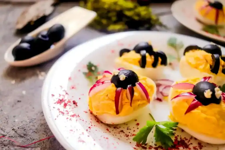 Plate of gourmet deviled eggs garnished with black olives, red onions, and herbs on a speckled plate.