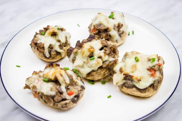 Five stuffed mushrooms topped with melted cheese on a white plate.