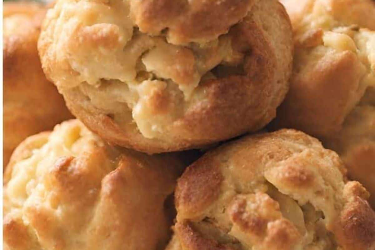 A plate of Gougeres served on a wooden table, with a piece of cheese visible to the side.