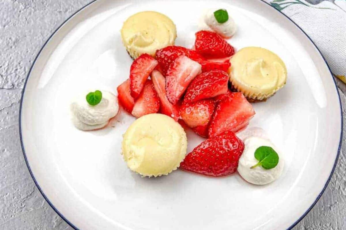 A white plate with strawberries and mini biscoff cheesecakes.
