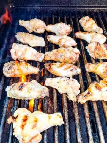 Chicken wings grilling on a barbecue on a black grill.