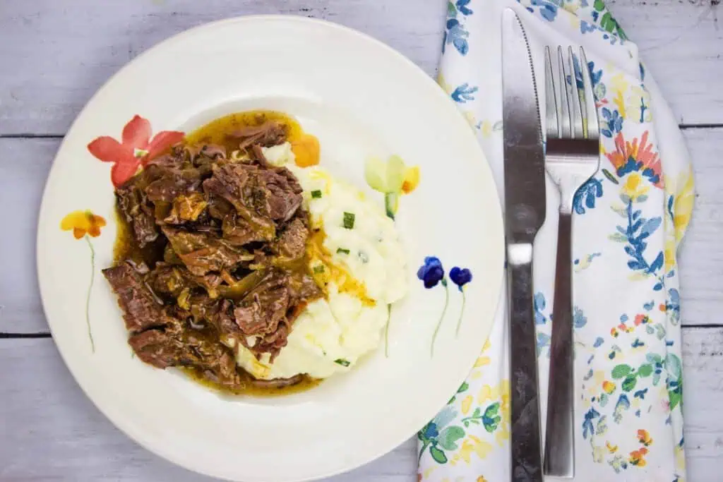 A plate of pot roast with bacon and mashed potatoes with gravy.