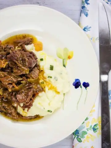 A plate of pot roast with bacon and mashed potatoes with gravy.