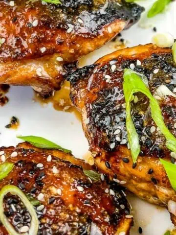 Three pieces of Air Fryer Honey Garlic Chicken garnished with sesame seeds and chopped green onions on a white rectangular plate.