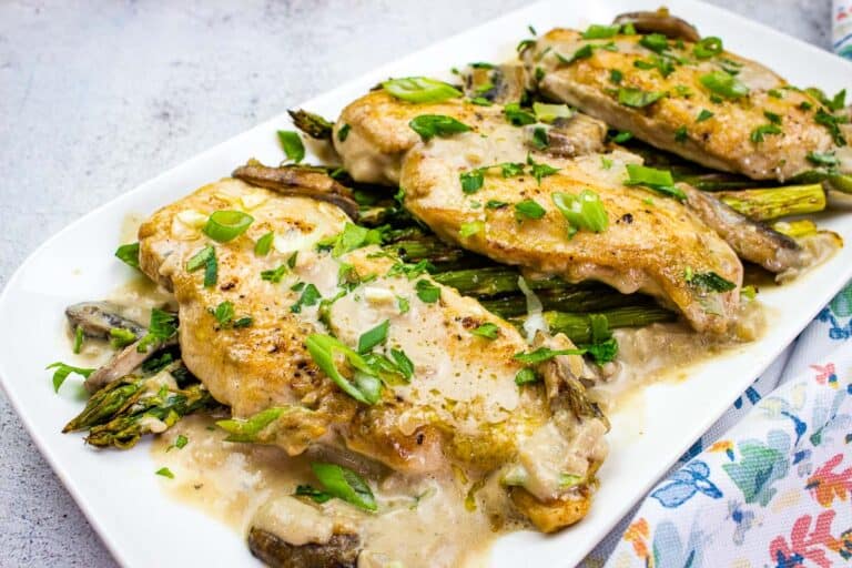 Plate of creamy chicken and asparagus garnished with green herbs and sliced green onions on a white rectangular dish.