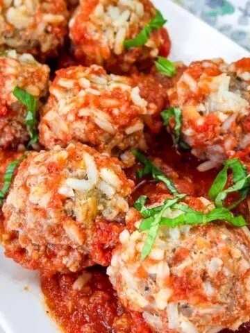 A white rectangular plate with several meatballs covered in tomato sauce, garnished with chopped basil.