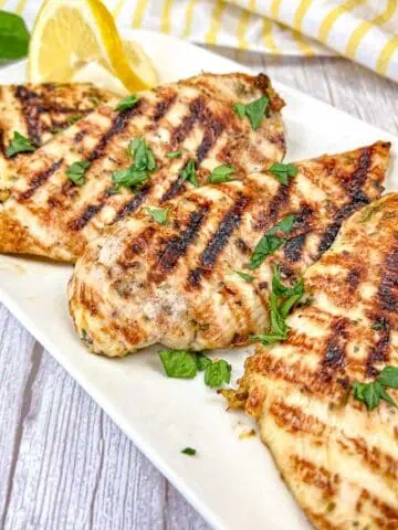 Four pieces of Ninja Woodfire Grill Lemon-Herb Chicken served on a white rectangular plate.