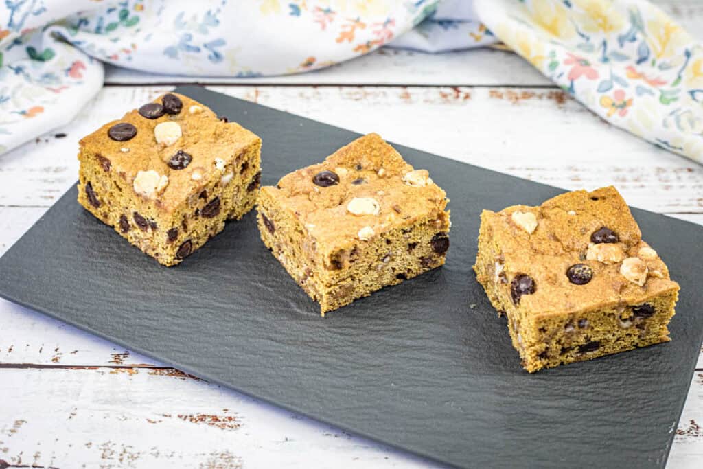 Three pieces of pumpkin blondies are arranged side by side on a black rectangular slate.