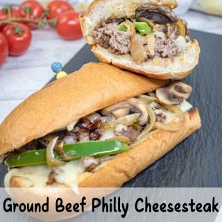 Ground beef Philly cheesesteak sandwich with green peppers, onions, and mushrooms, placed on a black slate.