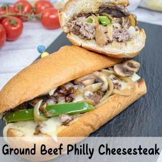 Ground beef Philly cheesesteak sandwich with green peppers, onions, and mushrooms, placed on a black slate.