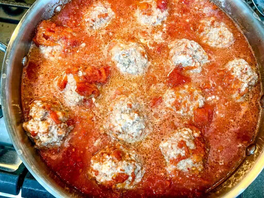 Meatballs cooking in a tomato-based sauce.