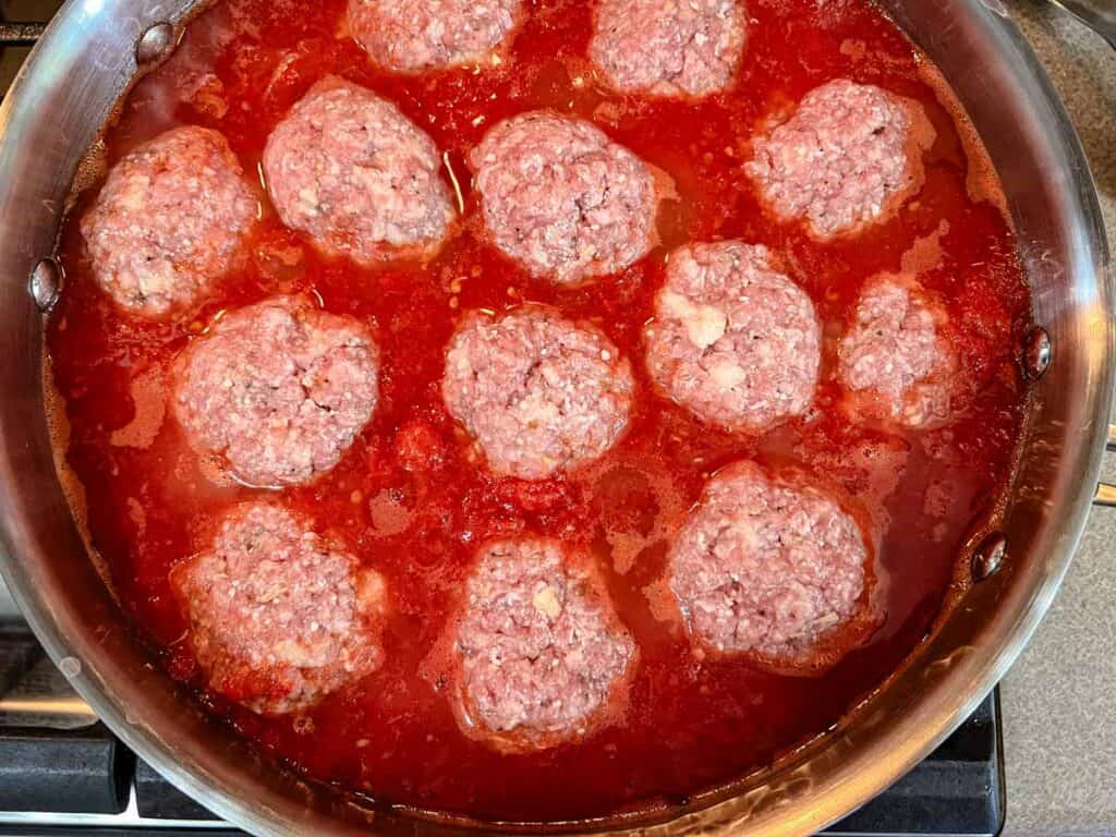 A pan containing giant meatballs in a tomato-based sauce is placed on a stovetop.