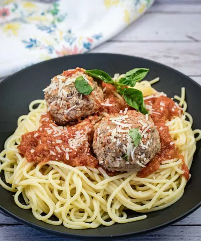 A plate of spaghetti topped with tomato sauce, two large meatballs, grated cheese, and a sprig of basil.