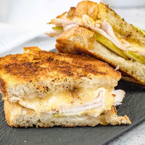 Two halves of a Turkey & Apple Grilled Cheese on a slate plate.
