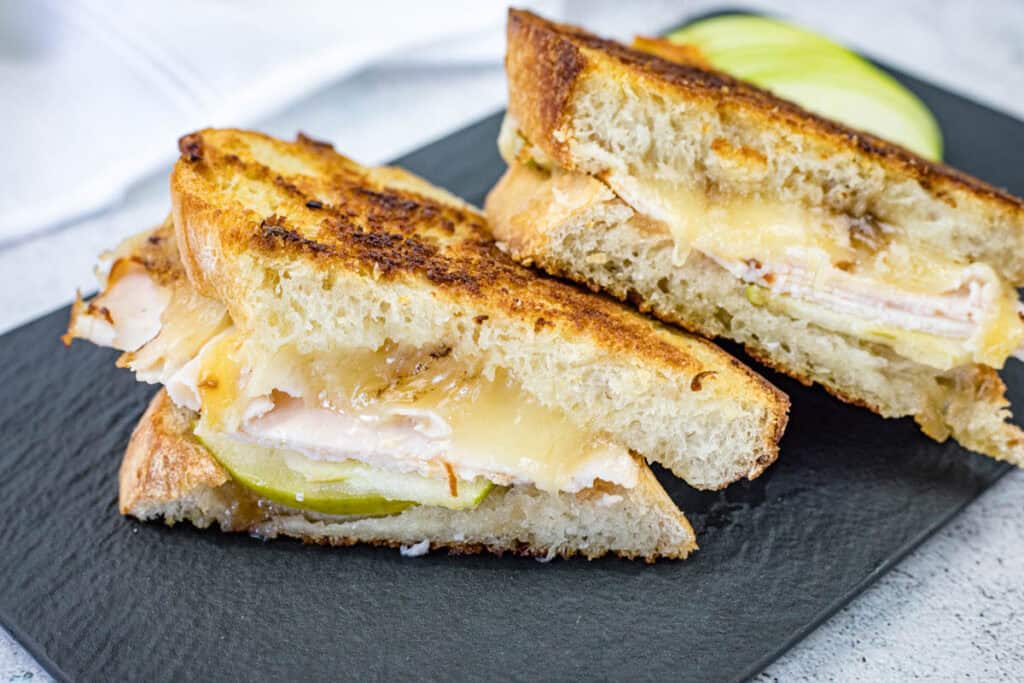 Turkey & Apple Grilled Cheese are placed on a black rectangular plate.
