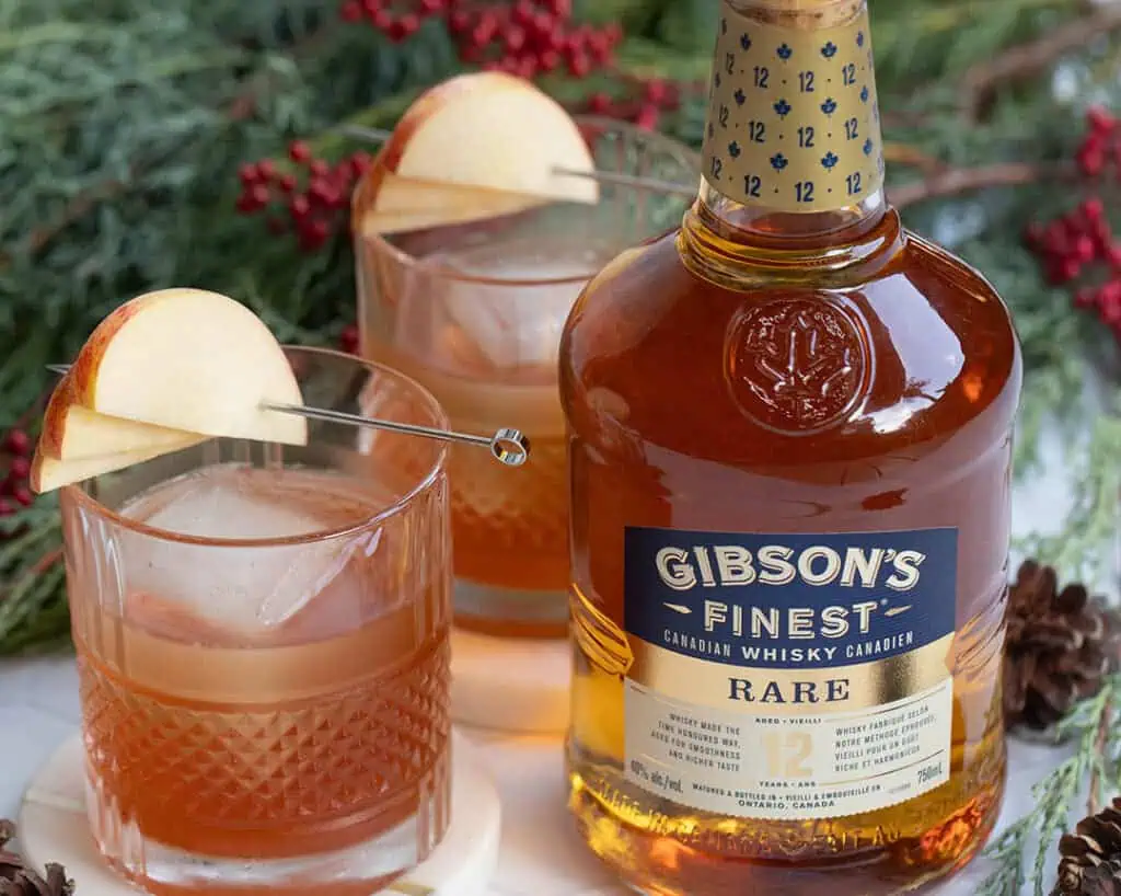 A bottle of Gibson's whisky with two glasses and apple on top.