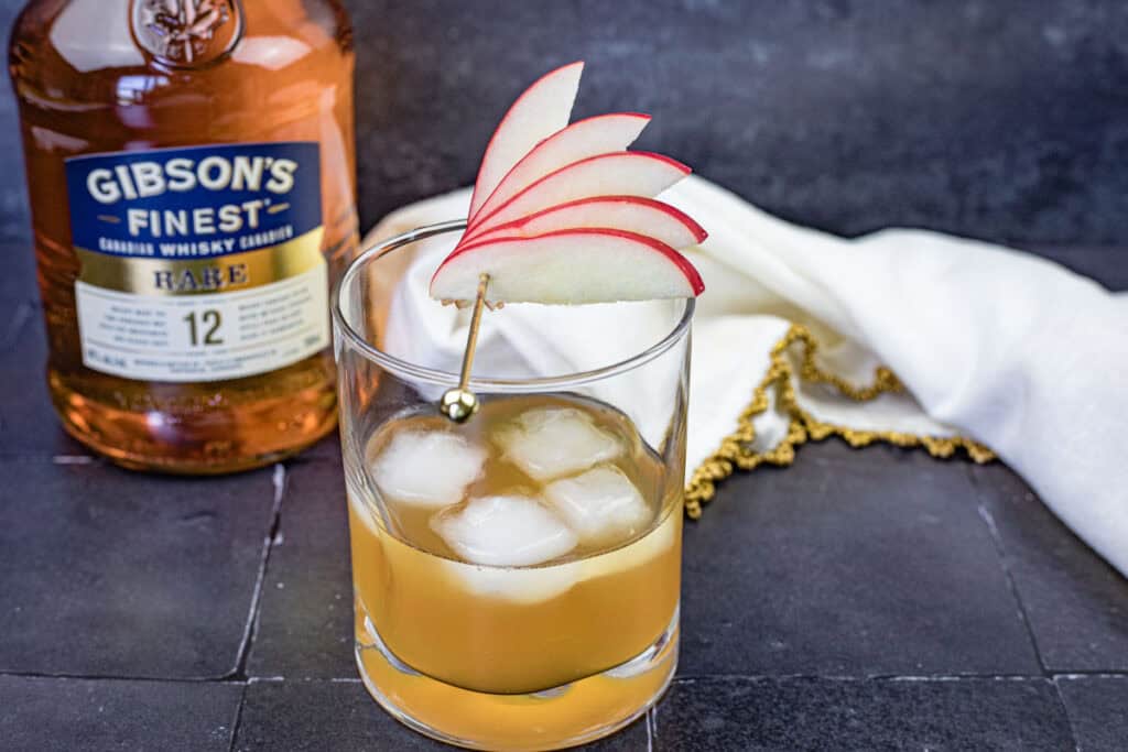 A glass of Gibson’s Apple Pie Old Fashioned with sliced apple on top.