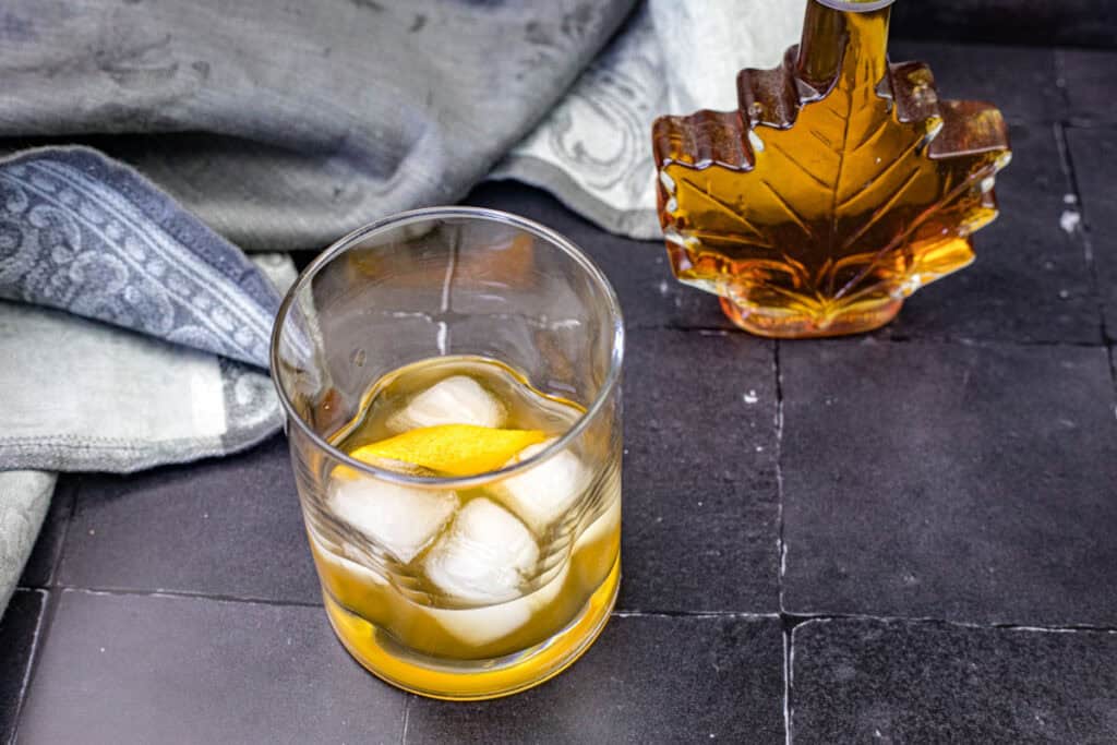 A glass of Grant&rsquo;s Smoky Maple Sour with a napkin and maple syrup on the background.