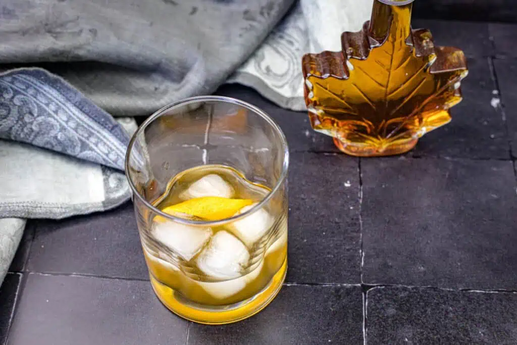 A glass of Grant’s Smoky Maple Sour with a napkin and maple syrup on the background.