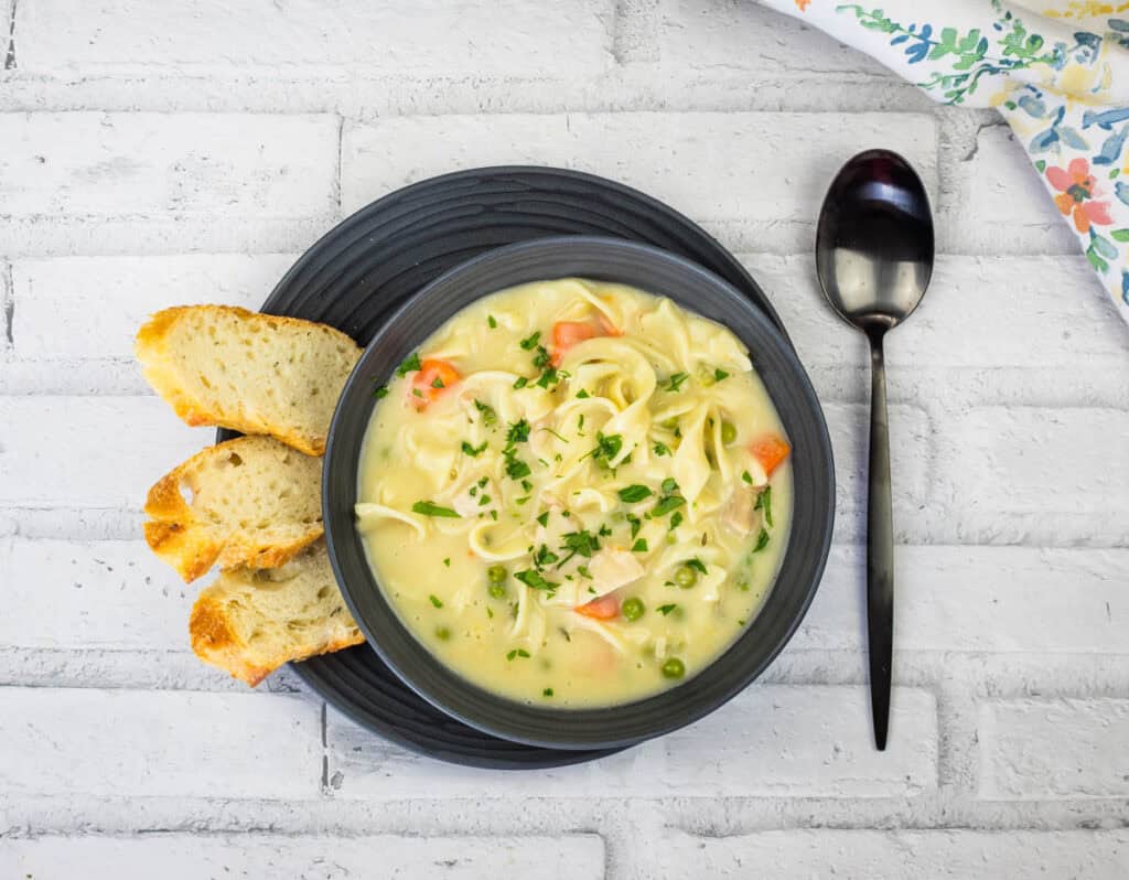 Top-down shot of Creamy Turkey Noodle Soup on a bowl with bread slices on a plate.