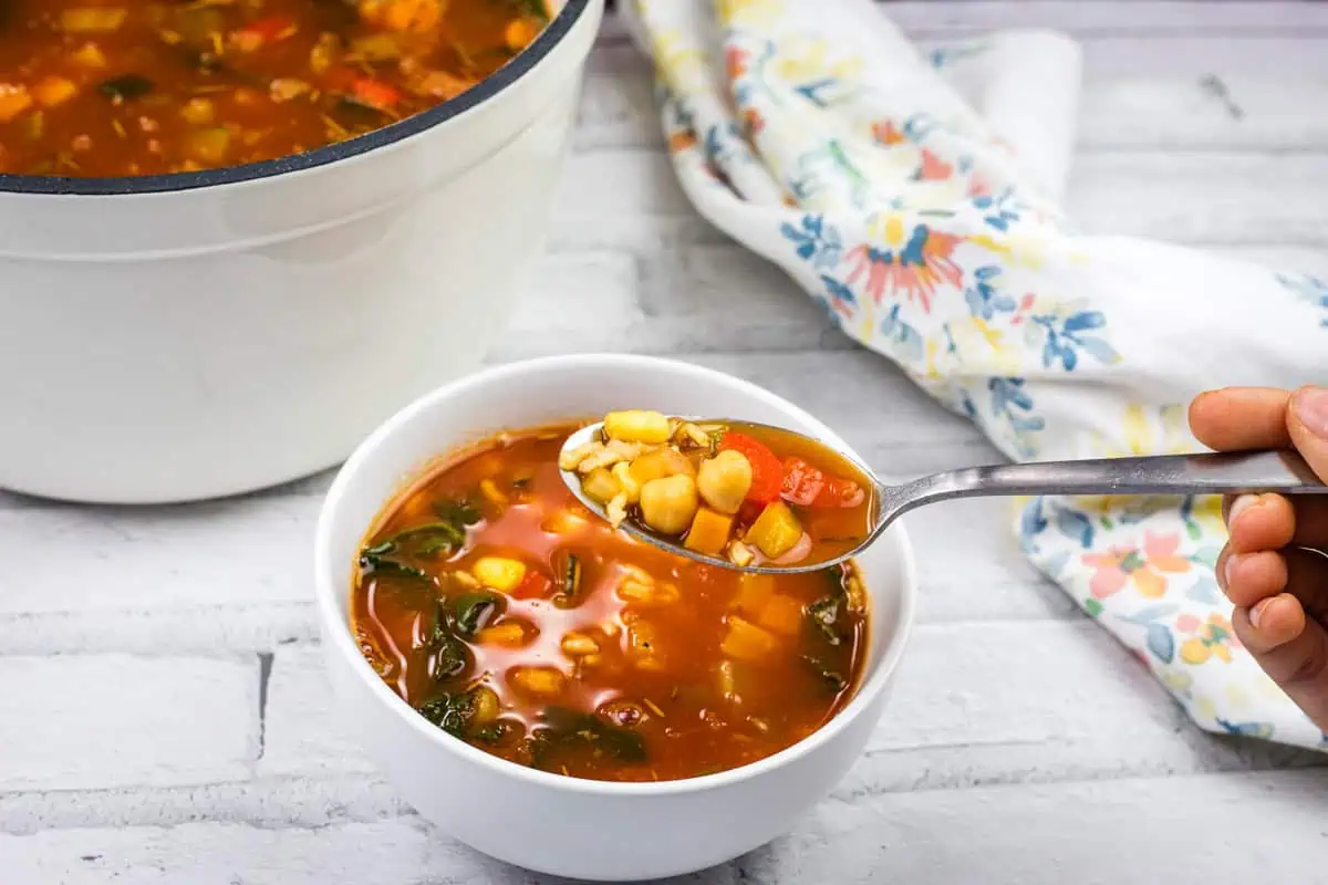 A bowl of Panera Bread’s 10 Vegetable soup with beans and greens on a white surface.