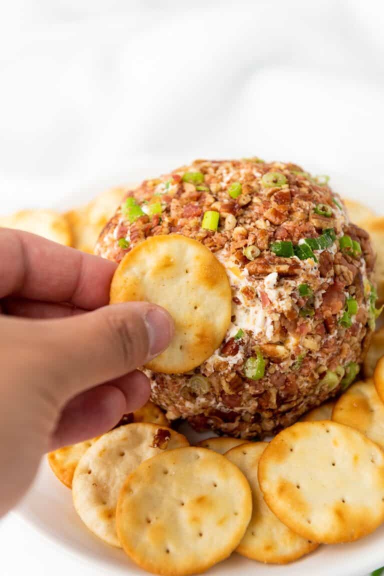 A hand holding a cracker getting a small amount of Pecan Bacon Cheeseball.