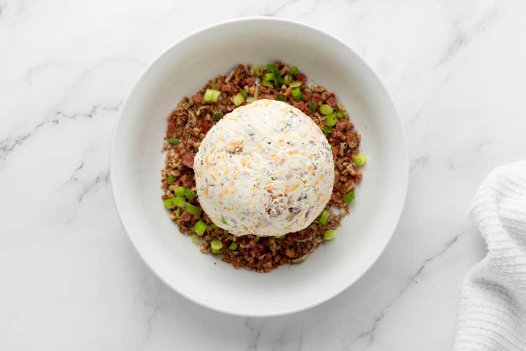 Roll the chilled cheeseball in the prepared coating mixture.